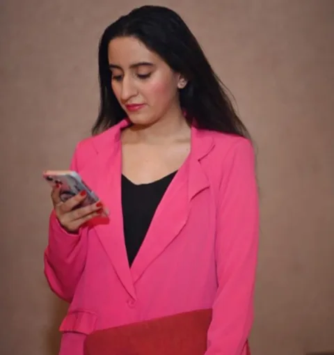 Sukoon in a pink blazer, looking at her phone